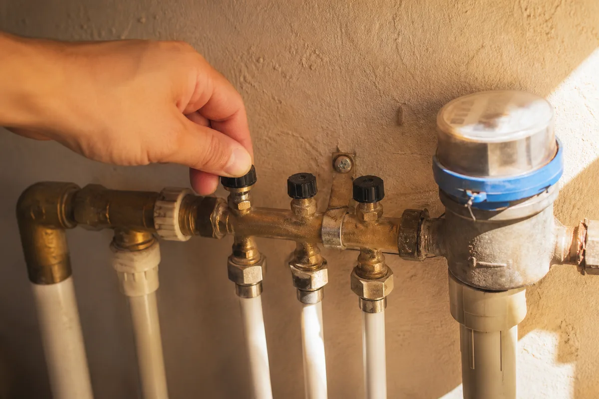 Main fermant le robinet d’arrêt général près d’un compteur d’eau