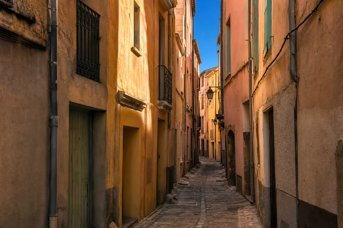 Ruelle du centre historique de Perpignan avec façades ocre et volets colorés sous une lumière méditerranéenne