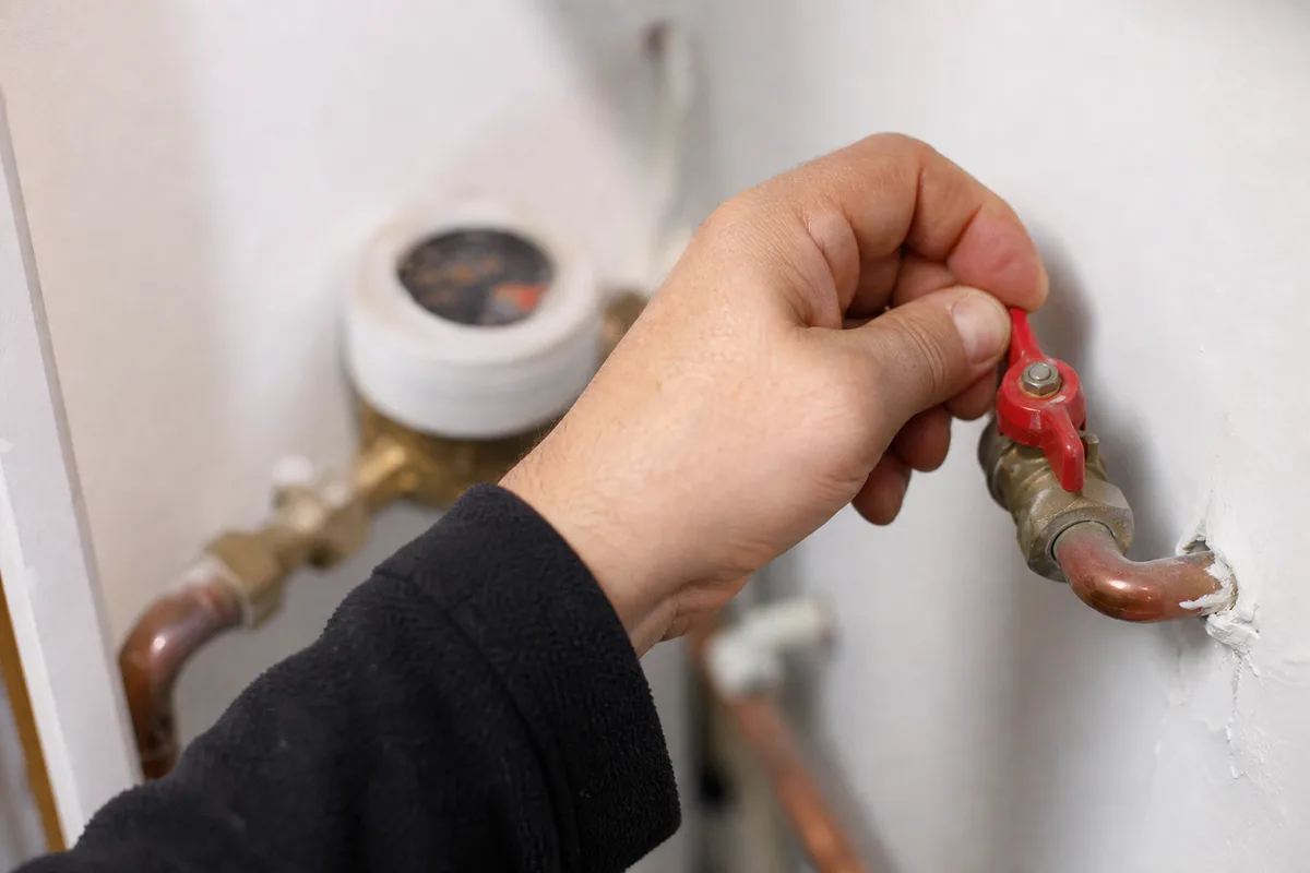 Main fermant une vanne d&rsquo;arrêt générale sur une canalisation en cuivre dans un placard technique